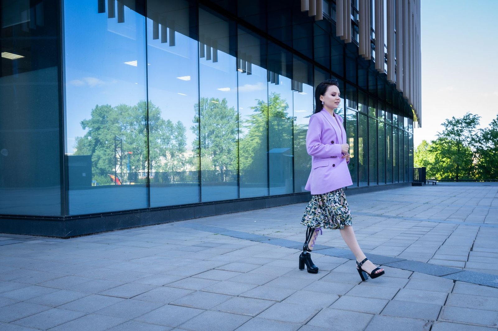Stylish woman with prosthetic leg walking past modern building on a sunny day, embracing confidence and independence.