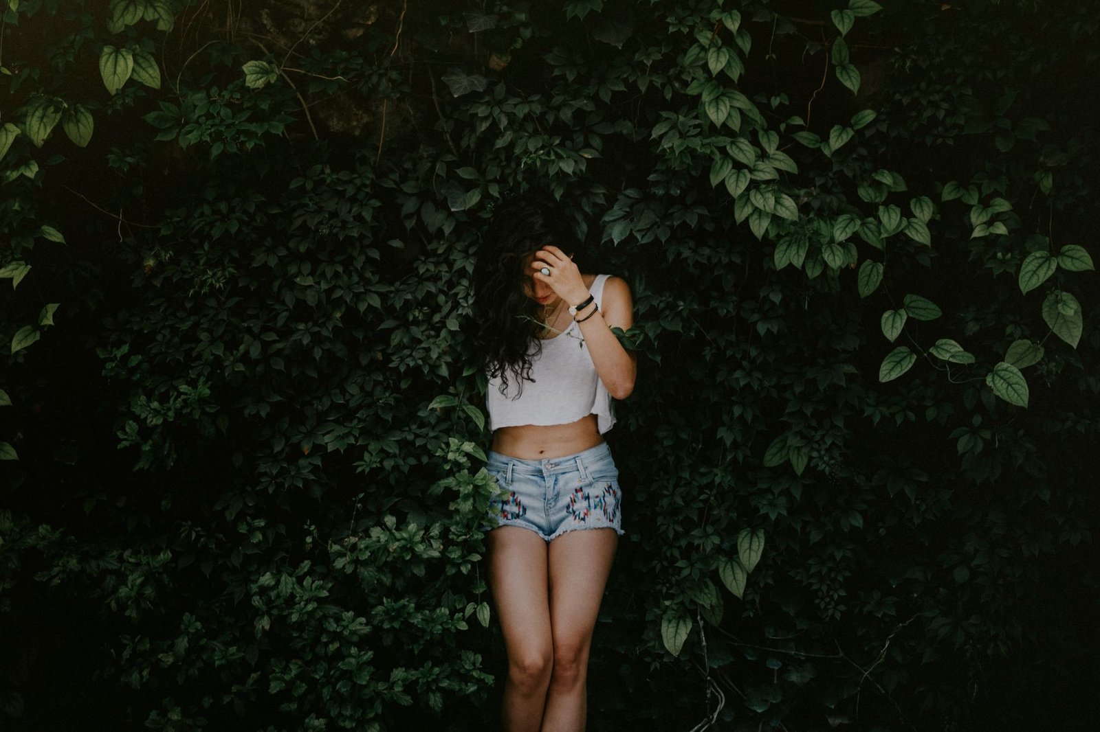 A woman in denim shorts stands against a lush green leafy background, creating a fashion-forward, nature-loving scene.