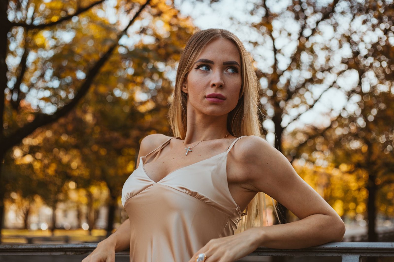 Stylish woman posing in autumnal Munich park with elegant expression.
