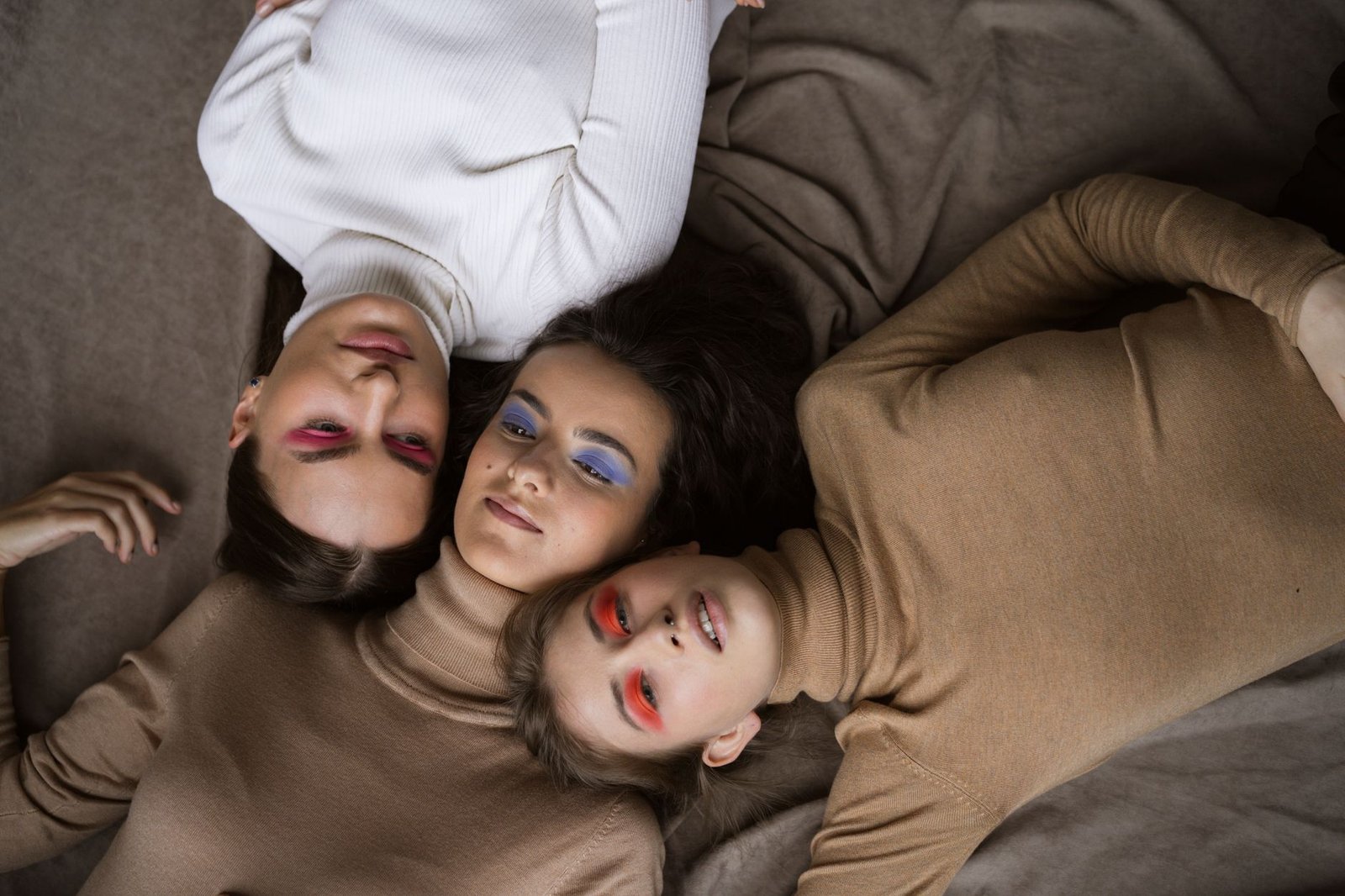 Three women with vibrant eye makeup lying in creative composition. Stylish and bold.