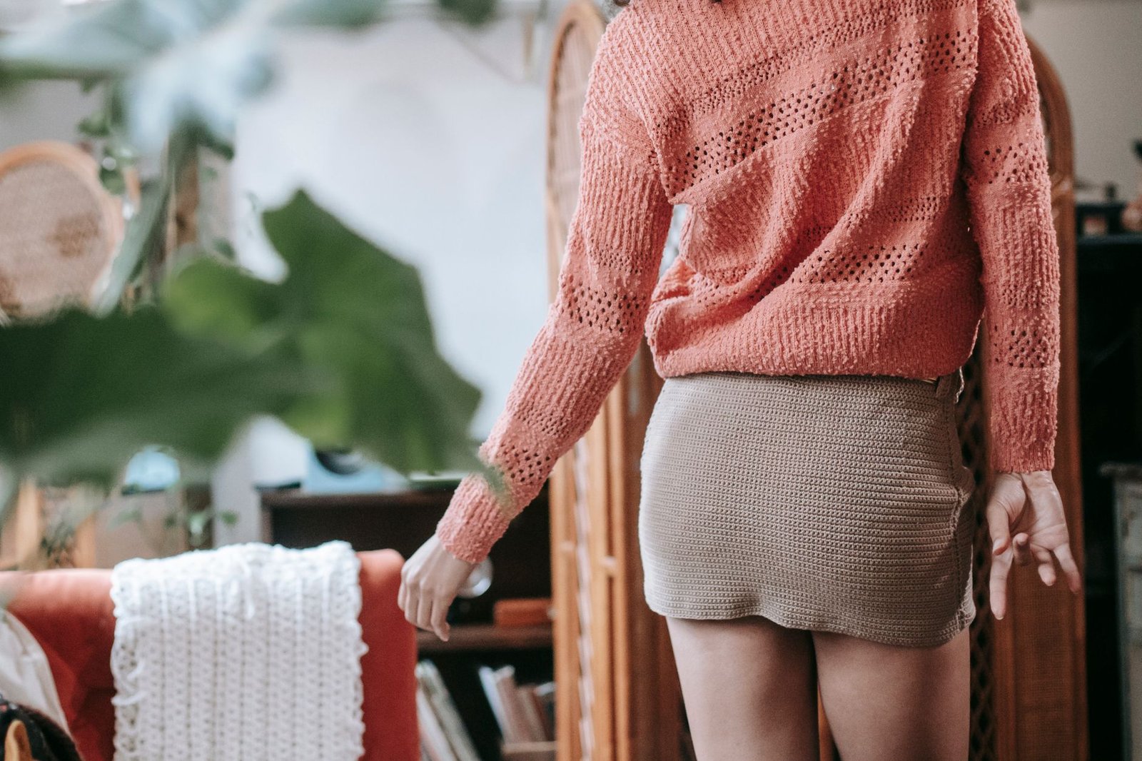 Crop unrecognizable female wearing beige knitted skirt and light orange sweatshirt touching armchair