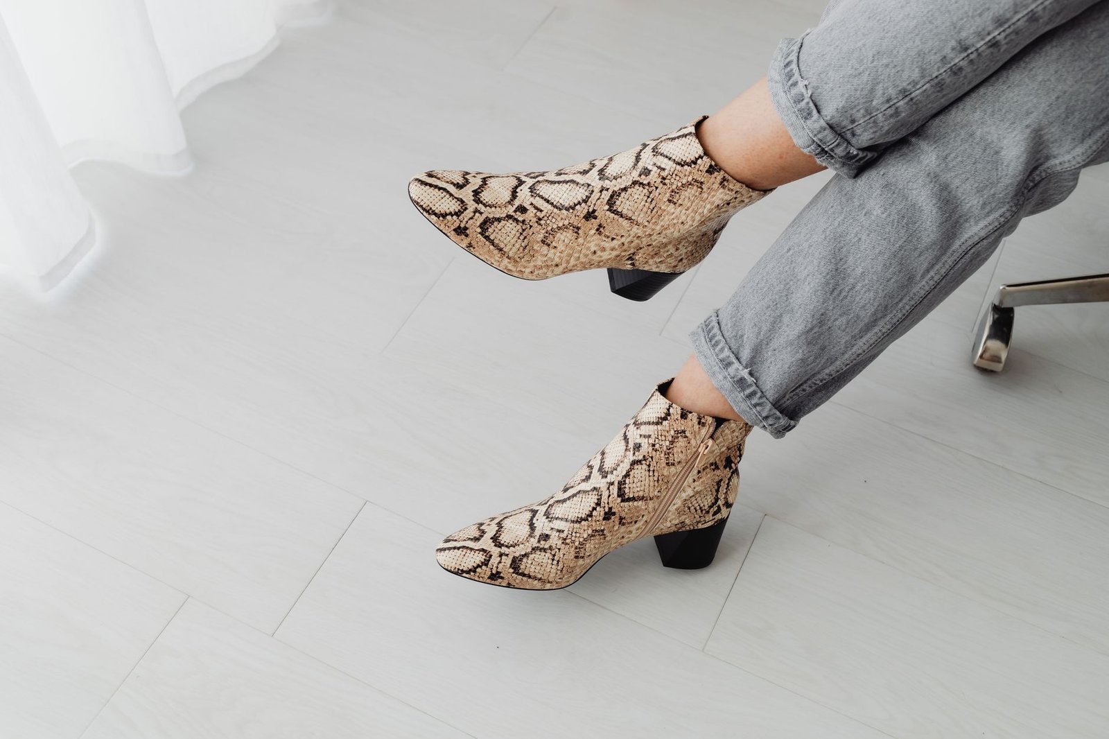 Stylish snake print boots paired with jeans on a light indoor floor.