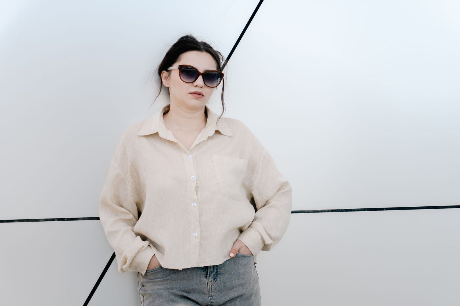 Trendy woman in sunglasses leaning against a geometric wall, showcasing fashion and confidence.