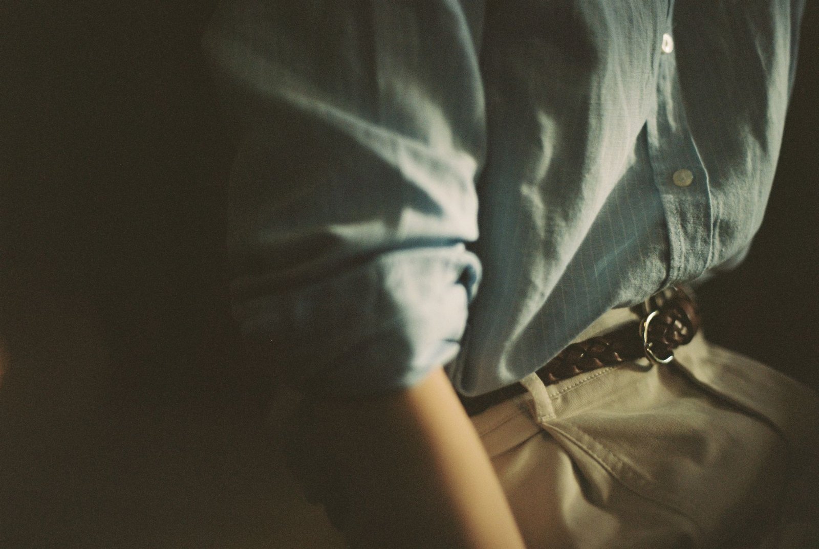 Close-up of a person's torso wearing a blue shirt with a braided belt and khaki pants.