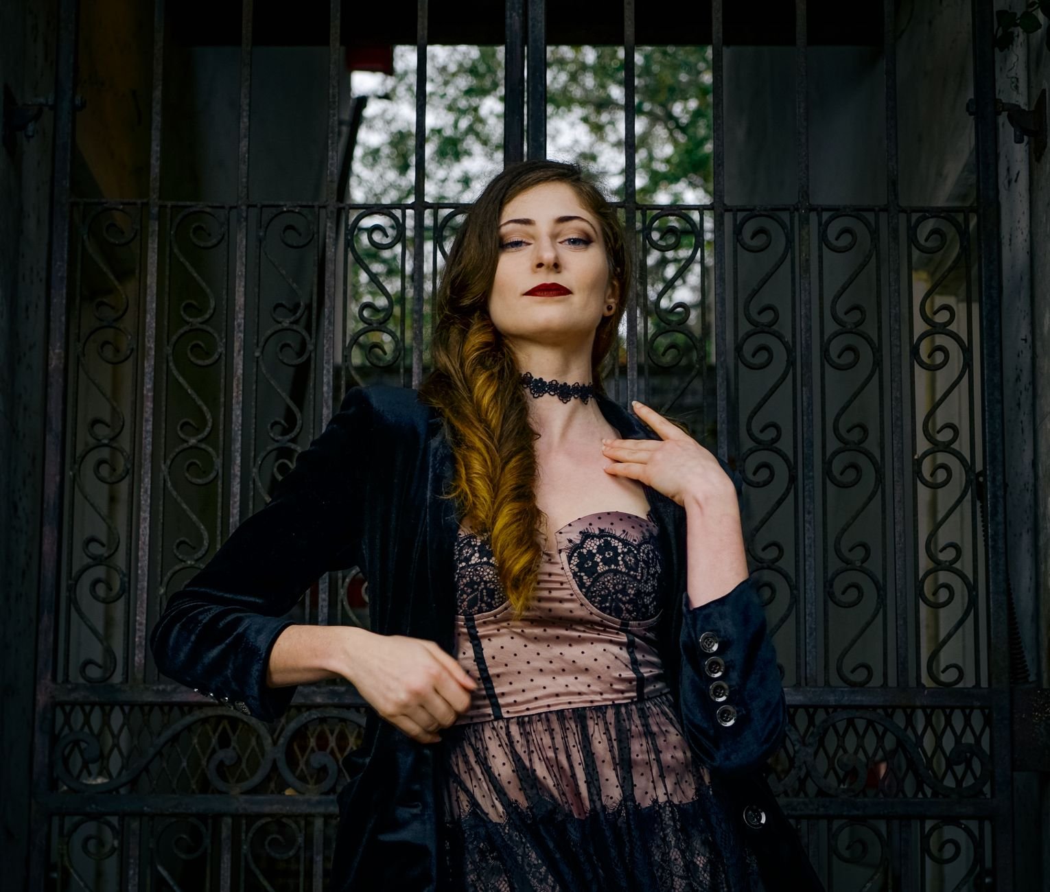 Fashionable woman in a black lace outfit poses confidently in front of an ornate gate.