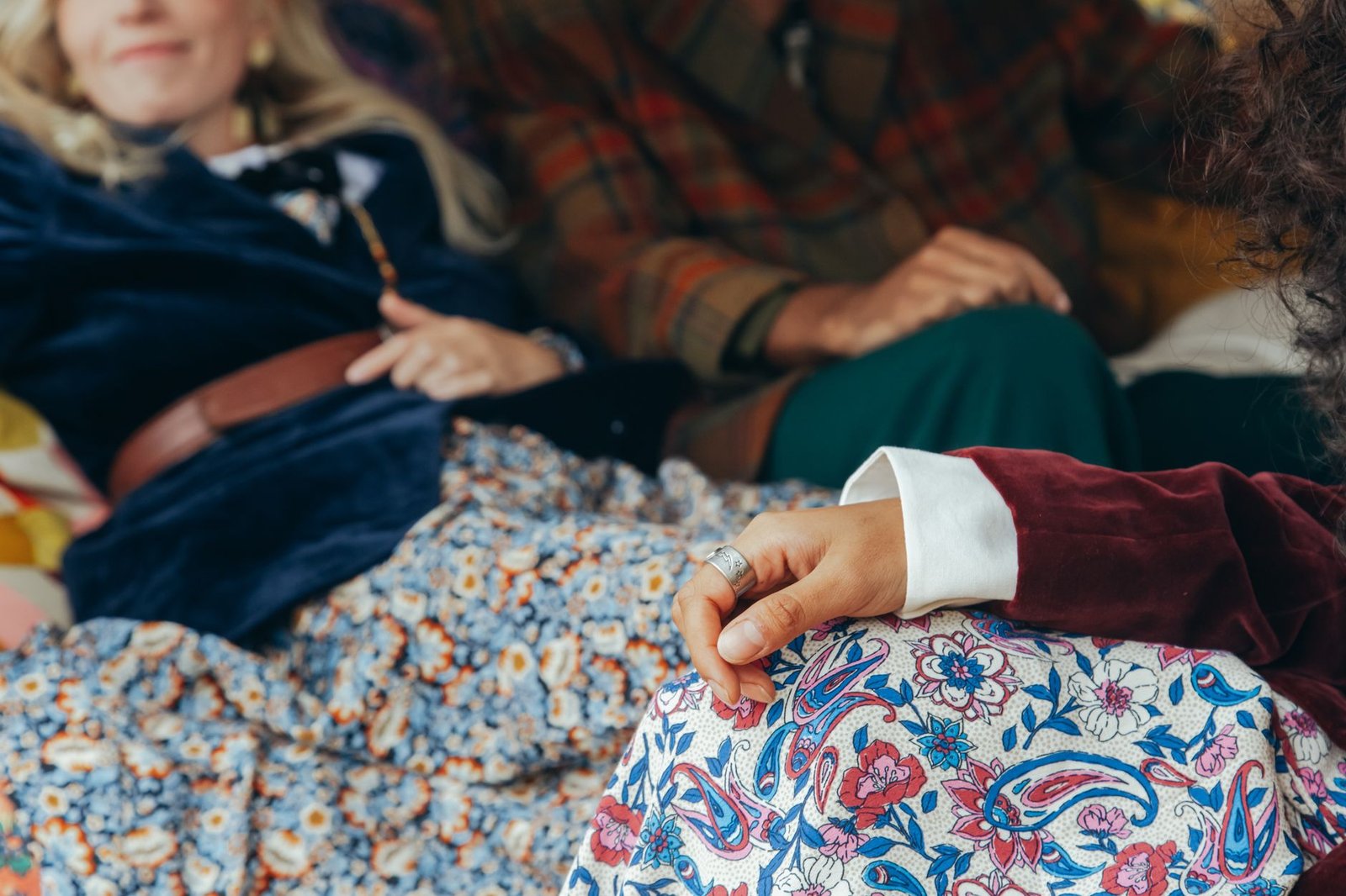 Close-up of a group wearing retro floral and plaid clothing, seated in a relaxed indoor setting.