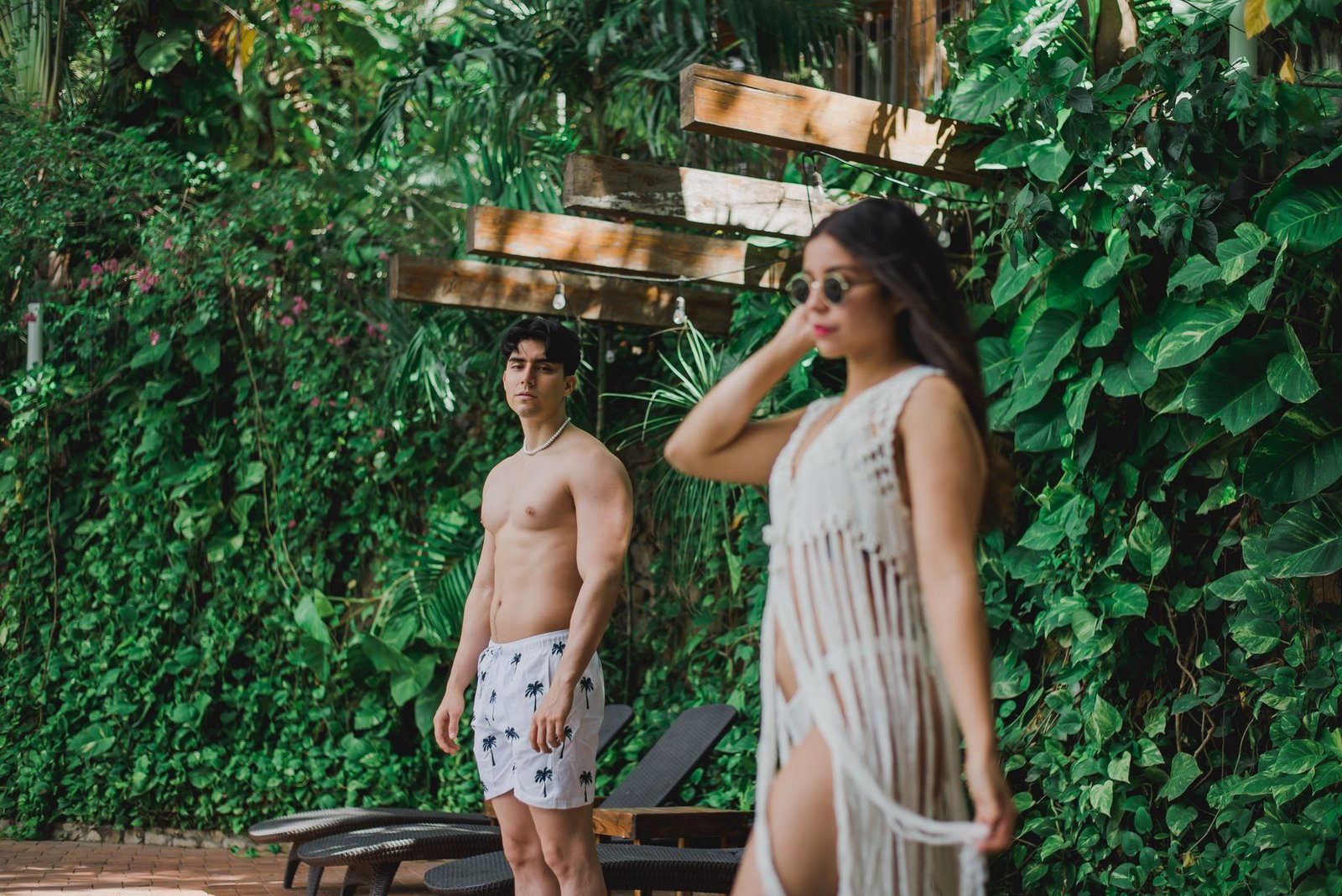 Stylish models posing in summer outfits by lush greenery in a tropical setting.