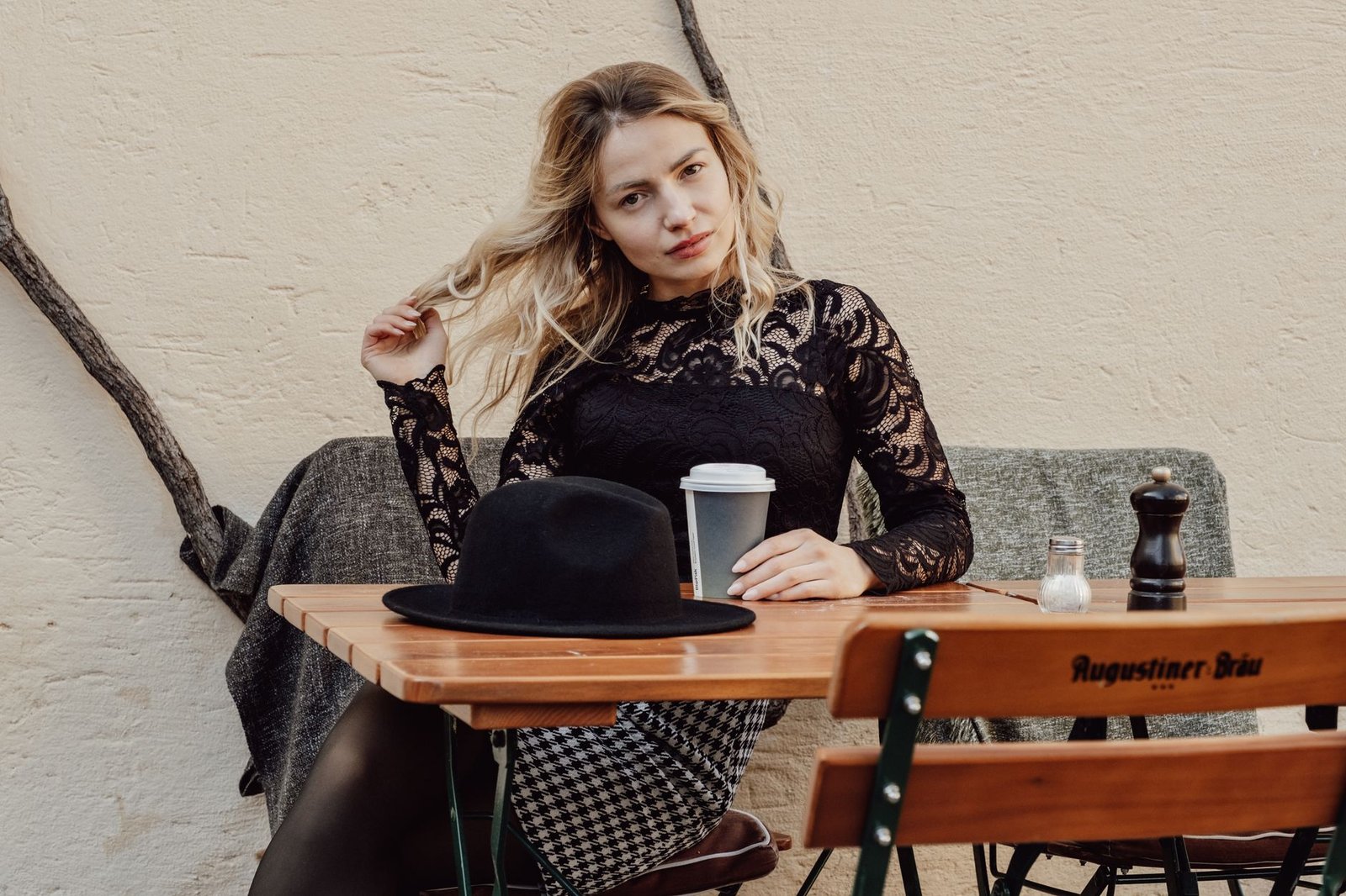 Chic woman in black lace blouse sitting at a café table with coffee, exuding style.