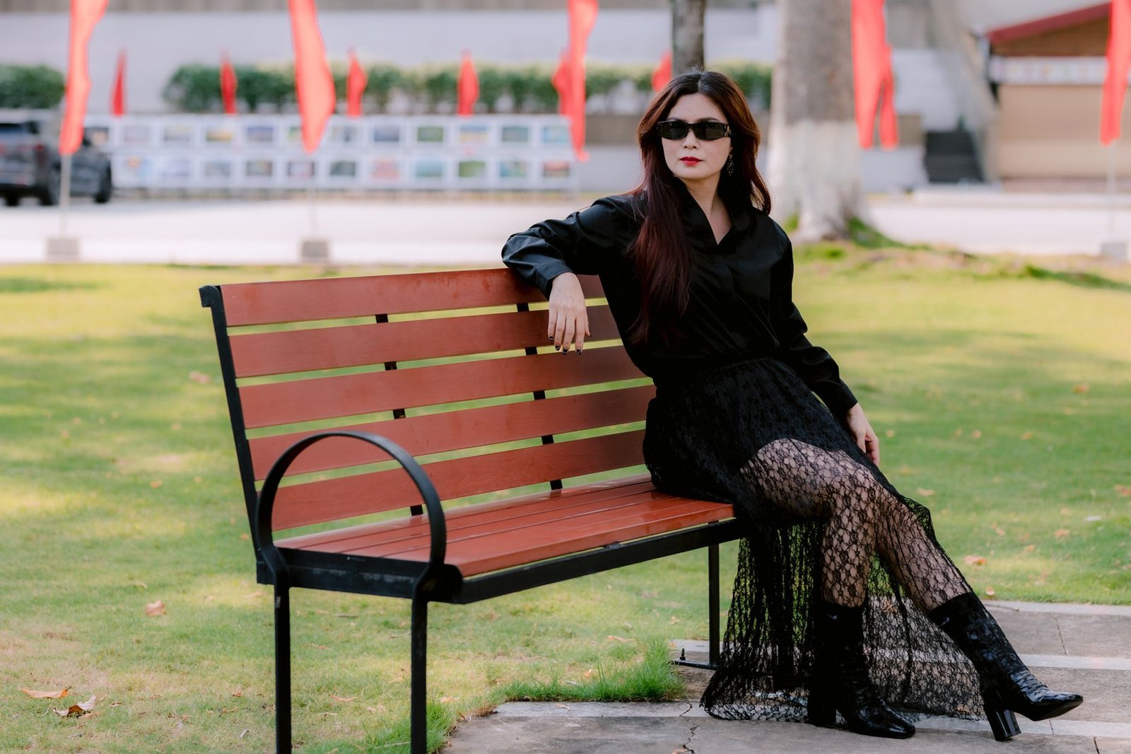 Stylish woman in black outfit and sunglasses relaxing on a park bench outdoors.