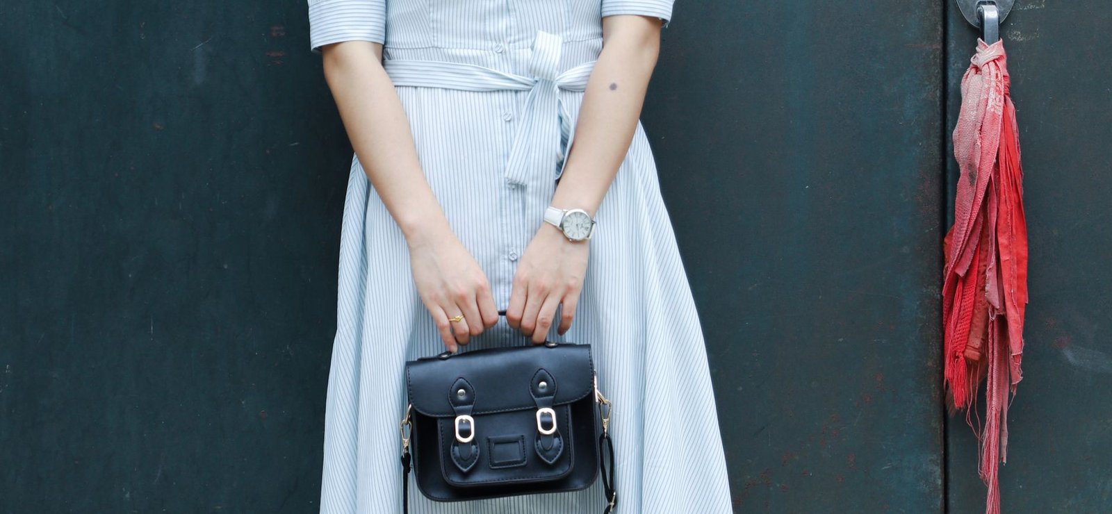 Stylish woman in a striped dress holding a leather handbag against a green door background.