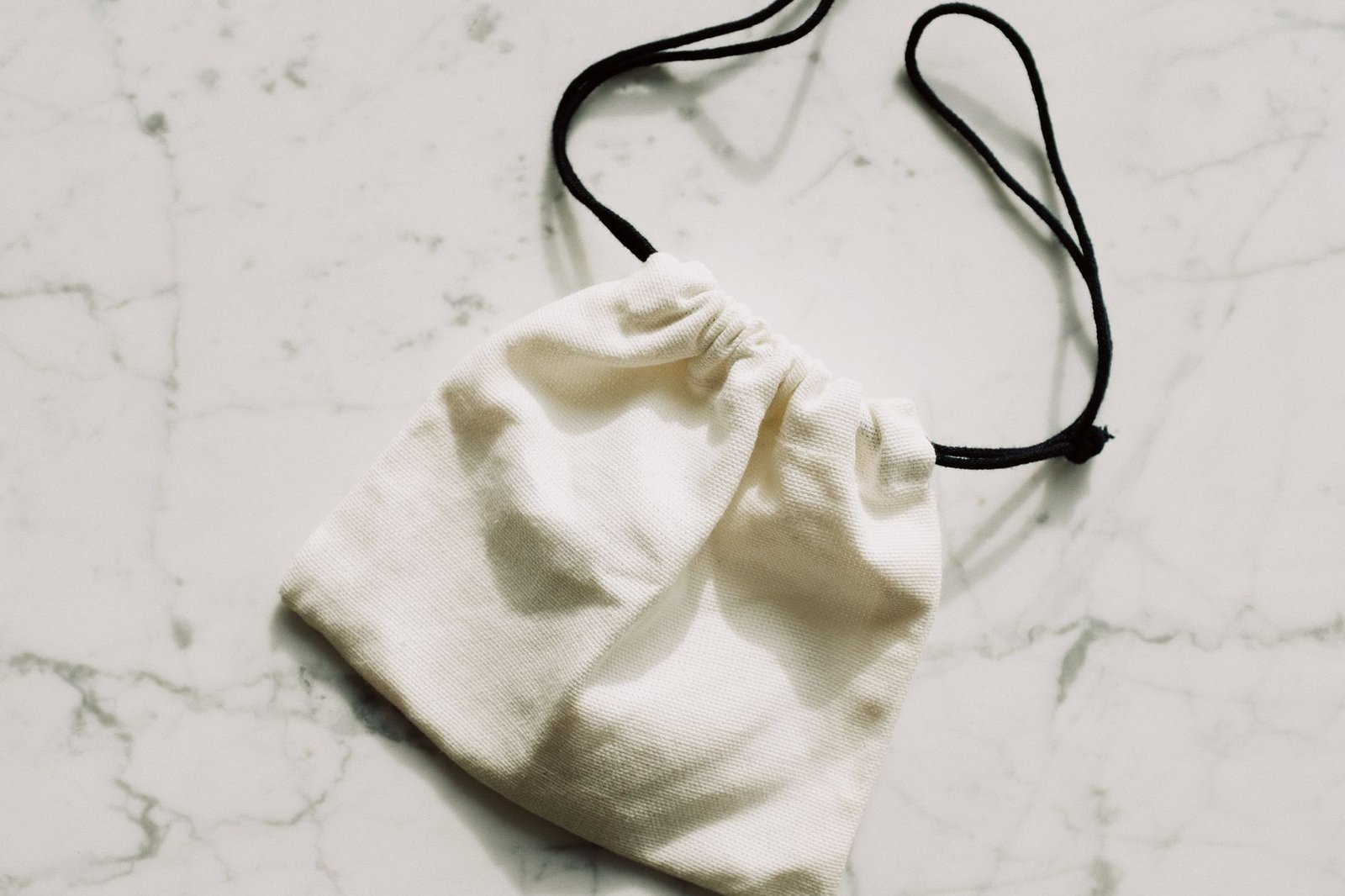 Simple white canvas pouch with drawstring on marble background. Perfect for storage.