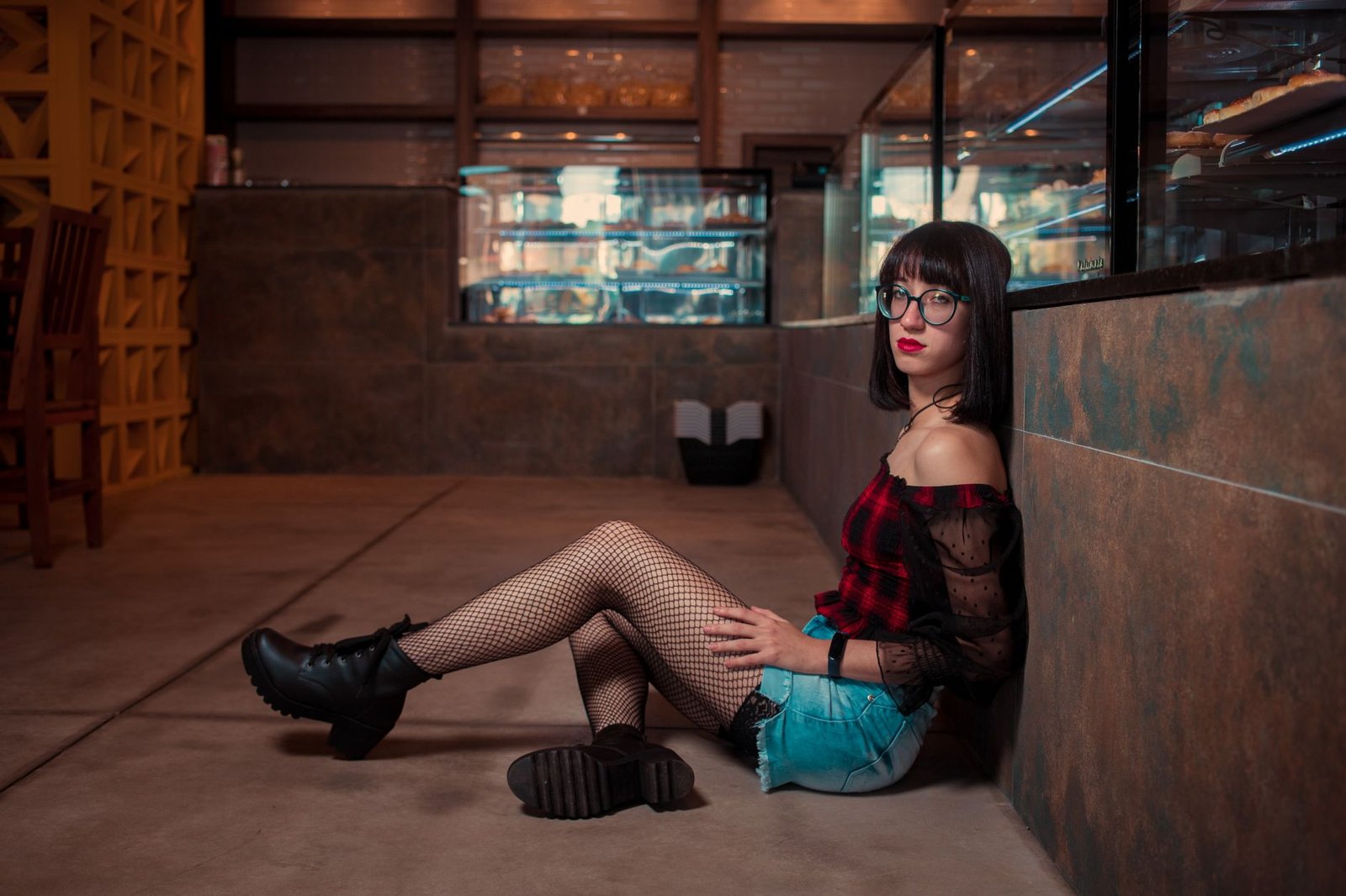 Trendy young woman sitting indoors wearing stylish outfit and glasses.