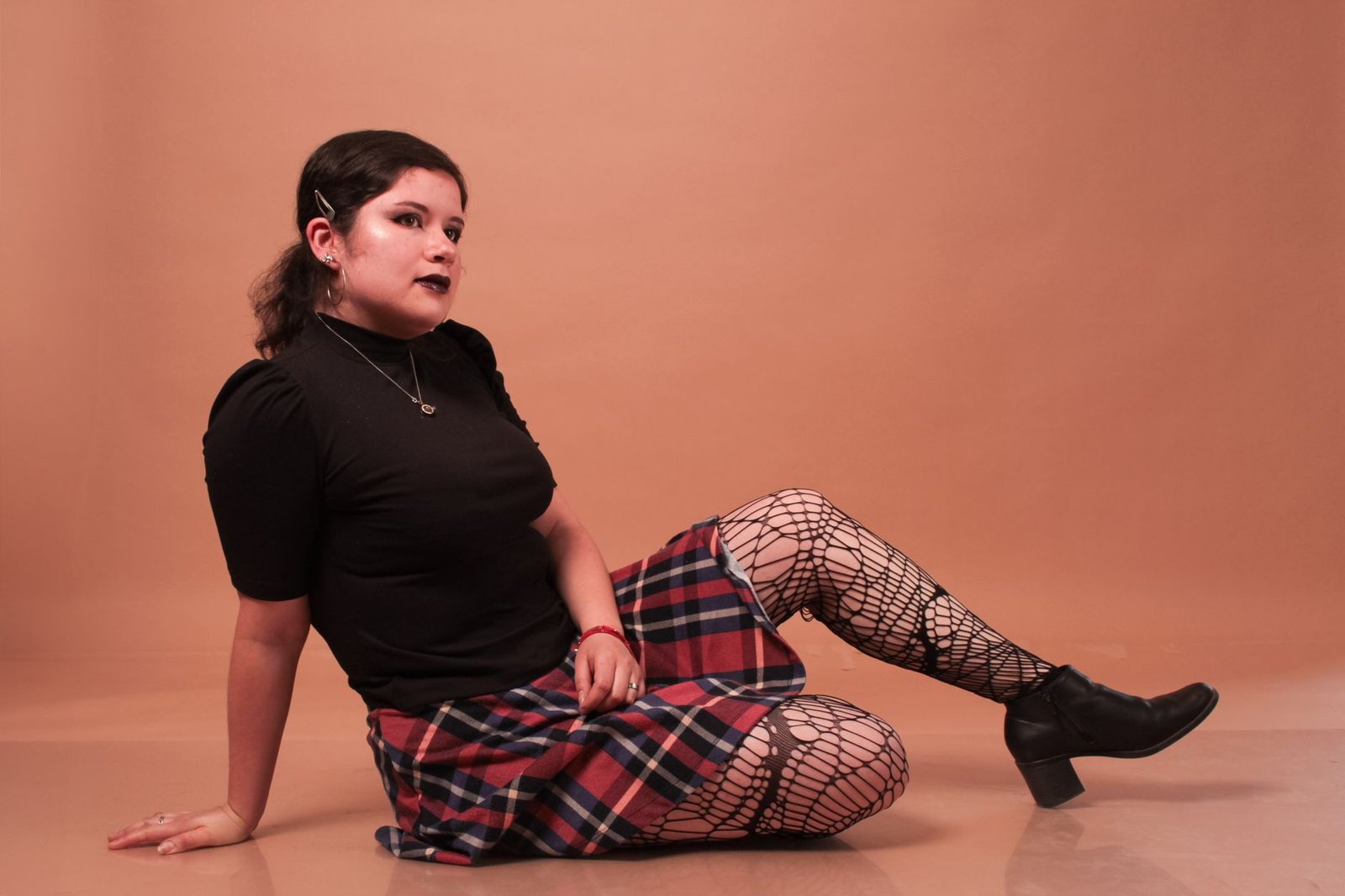 Stylish woman in a plaid skirt poses confidently in a studio setting, exuding a chic vibe.