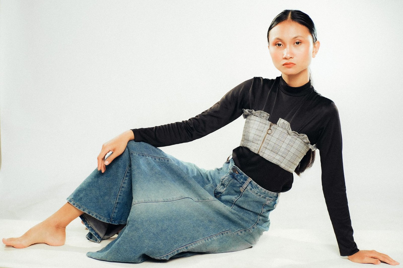 Female model posing in stylish denim and plaid outfit against a white studio background.