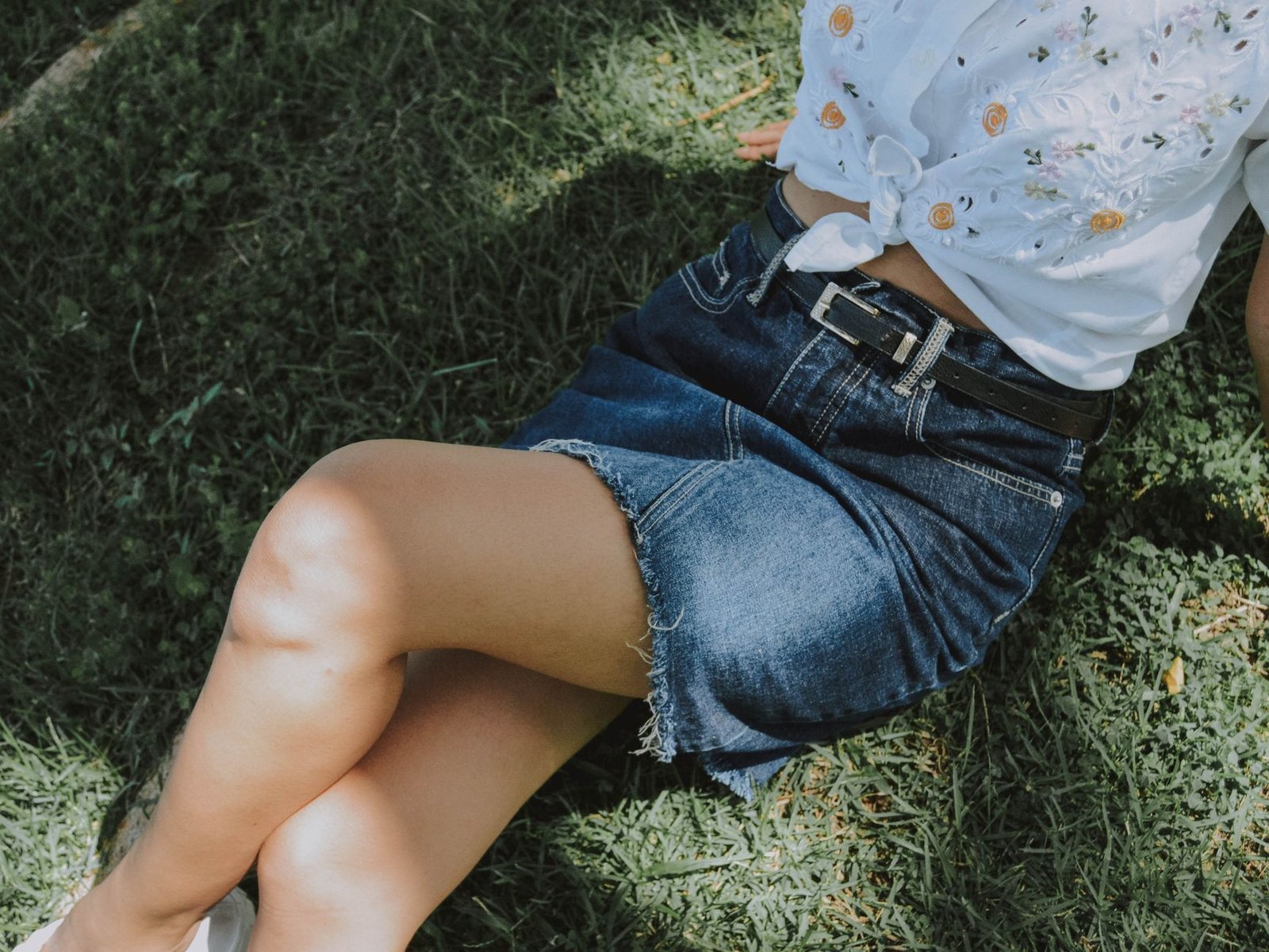 A woman in a denim skirt relaxes on grass, enjoying the sunshine.