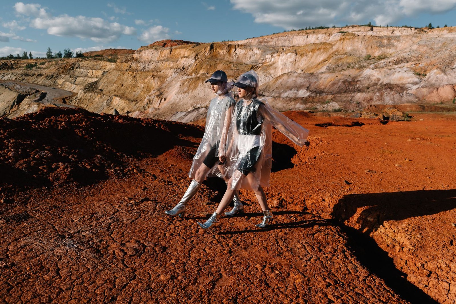 Two women in transparent raincoats walk across a striking desert landscape.