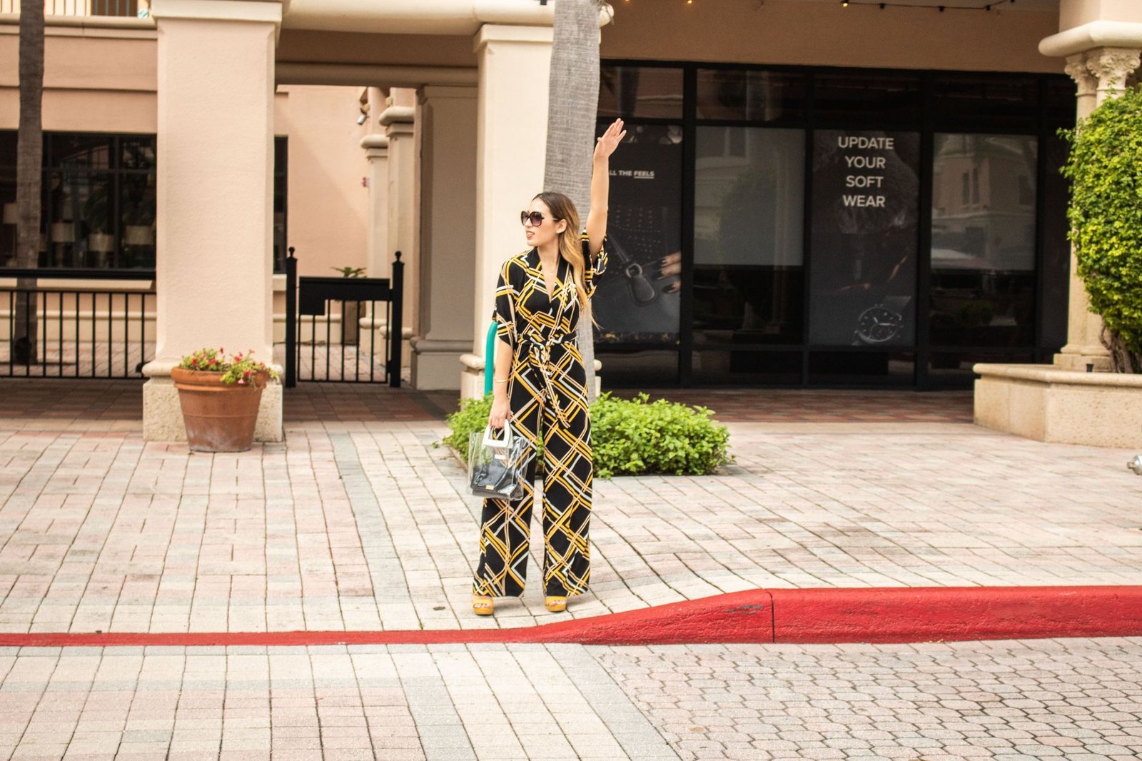 Stylish woman in geometric jumpsuit hailing a cab on a city street.