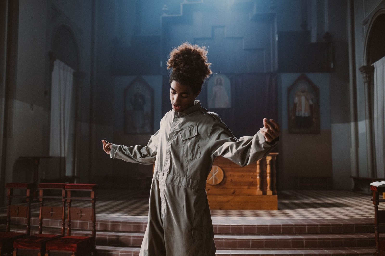 A young man in casual wear dancing inside a dimly lit church interior.