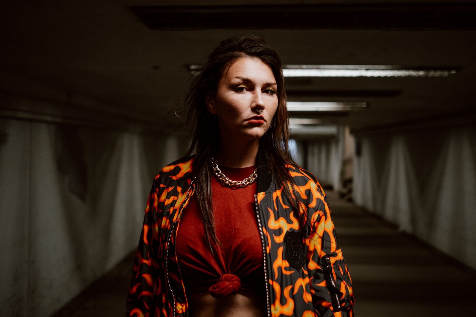 Edgy portrait of a woman with flame jacket and piercing in an urban tunnel.