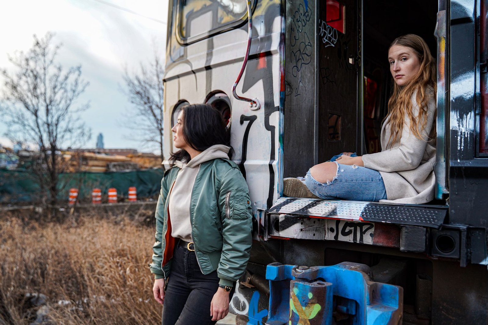 Stylish women posing by graffiti-covered train in NYC, capturing urban fashion vibes.