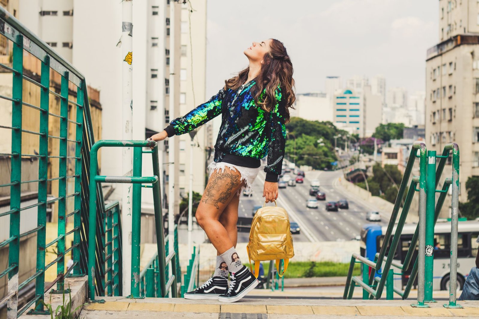 Fashionable woman with backpack posing on urban stairs in daylight city setting.