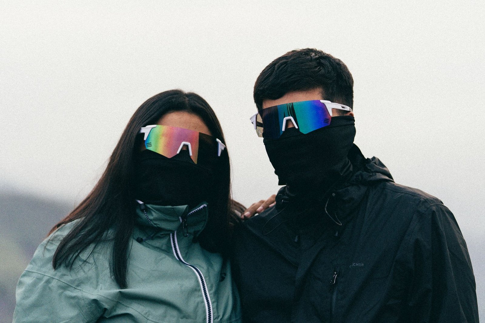 A couple wearing outdoor jackets and reflective sunglasses pose for a portrait.