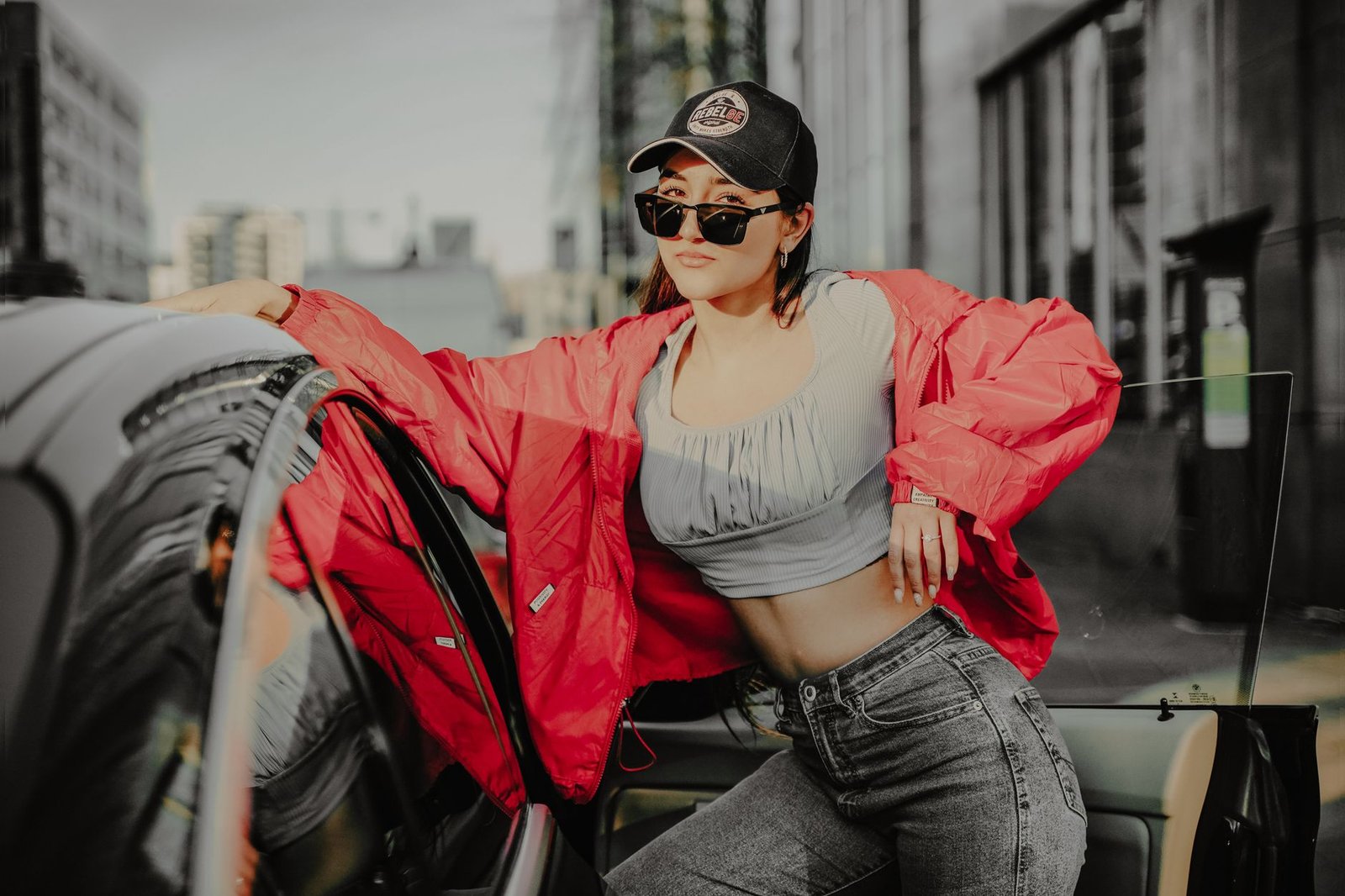 Fashion-forward woman in urban environment wearing cap and sunglasses with a red windbreaker.