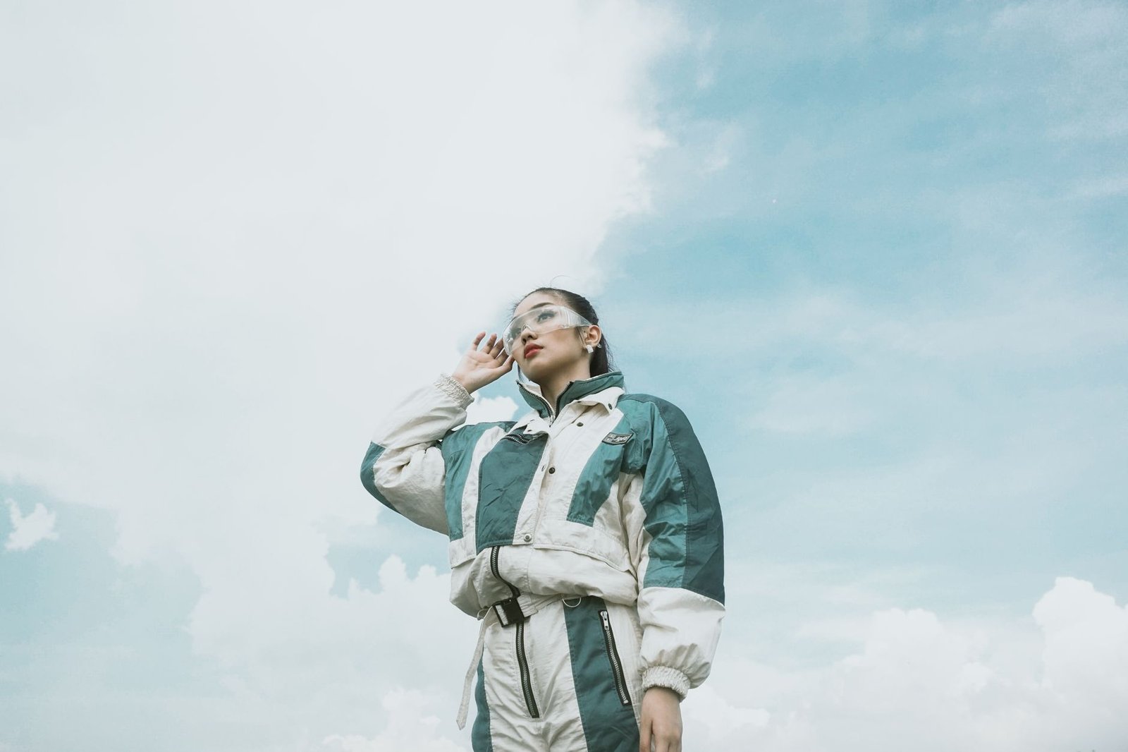 Stylish woman in a sporty outfit gazes into the distance with a vivid blue sky backdrop.