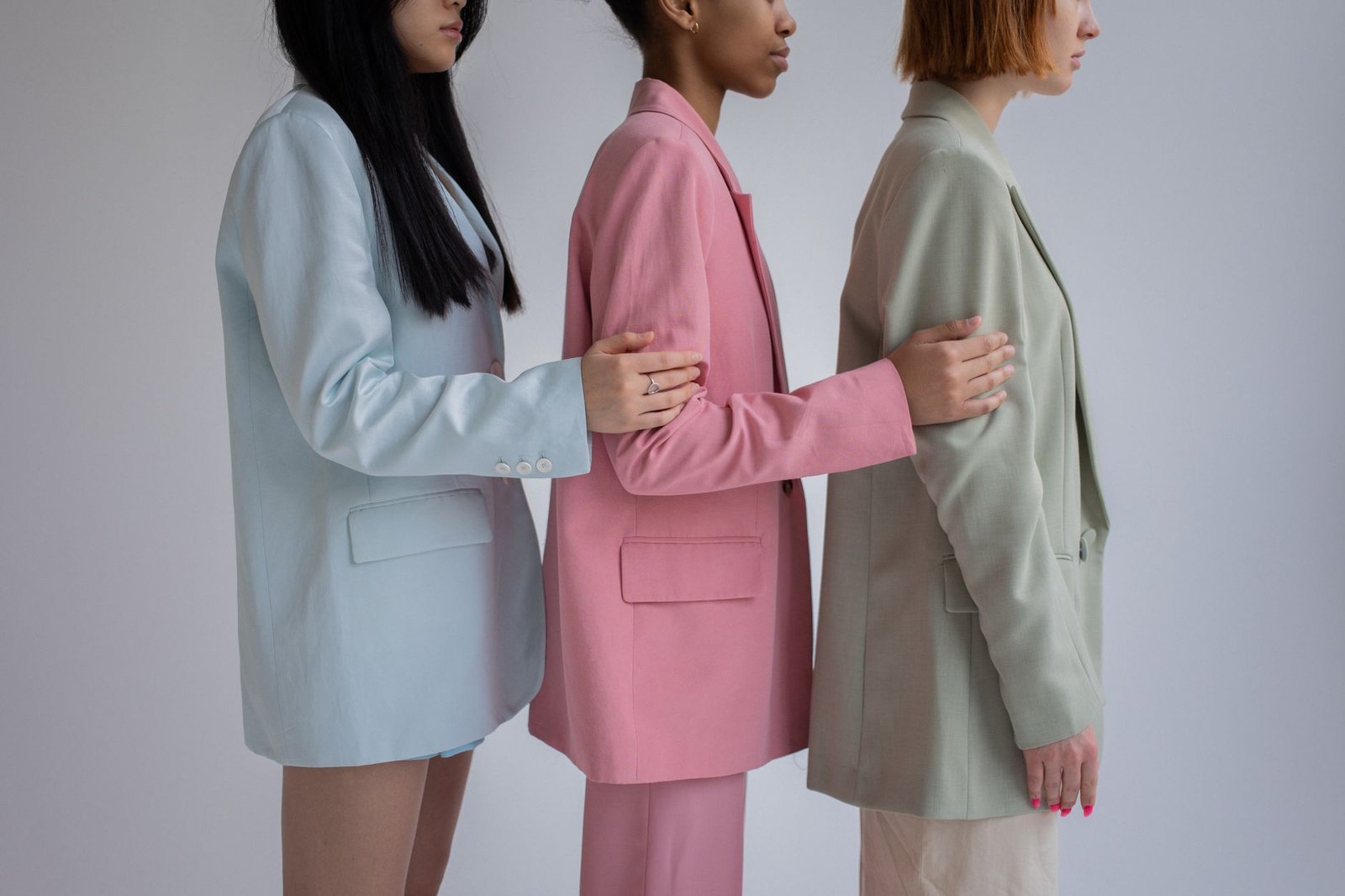 Side view of crop multiracial female models wearing trendy formal outfits standing in row against gray background