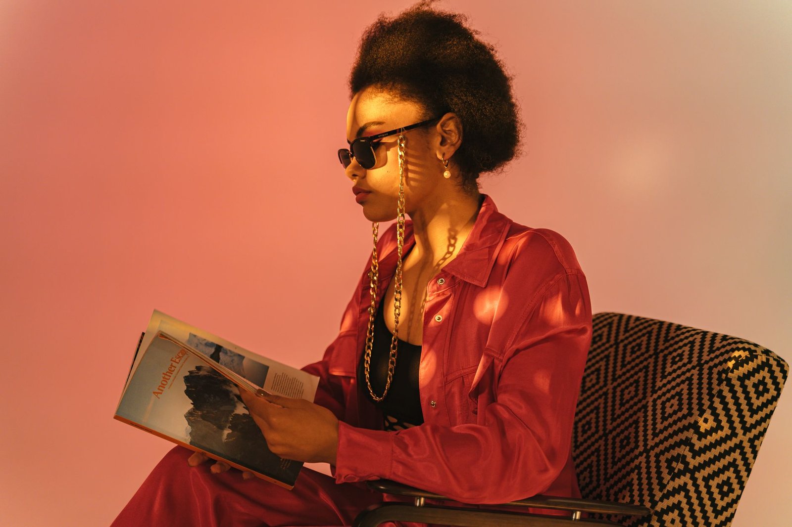 Fashionable woman with afro hair reading a magazine in a stylish studio setting.