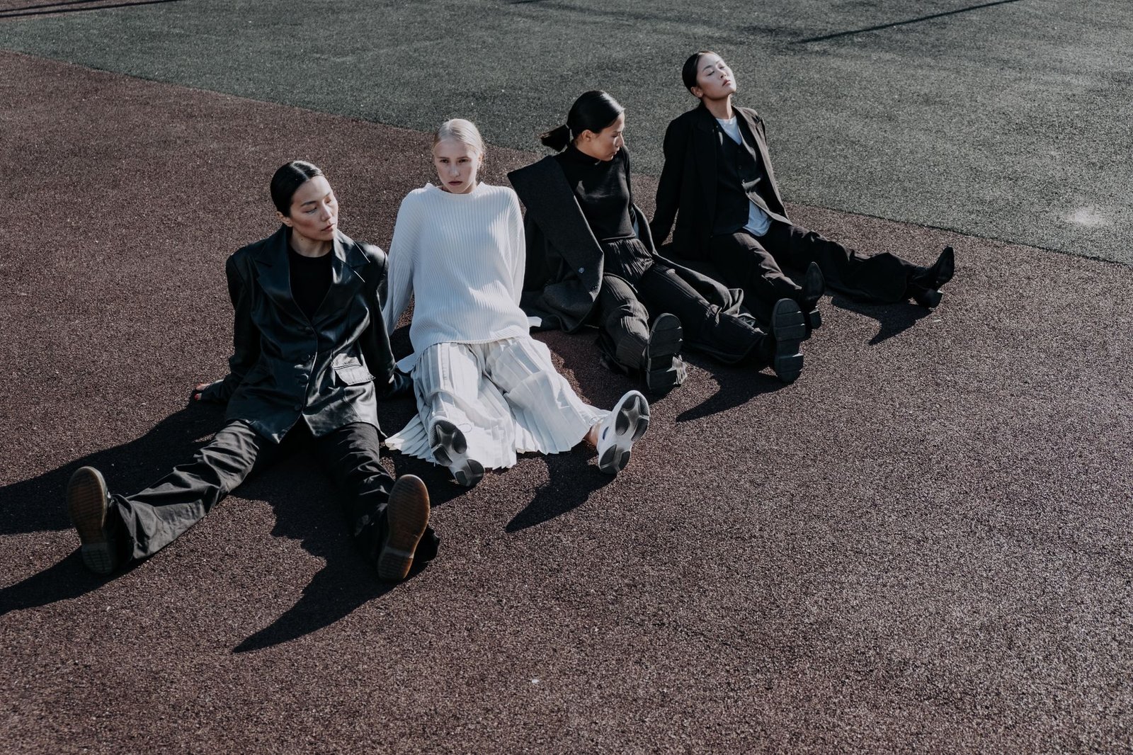 Group of stylish women in modern outfits sitting outdoors on a sports ground, embracing diversity and fashion.