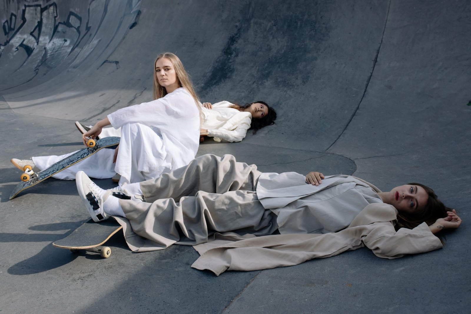 Trendy women in stylish outfits posing creatively with skateboards at an outdoor skate park.
