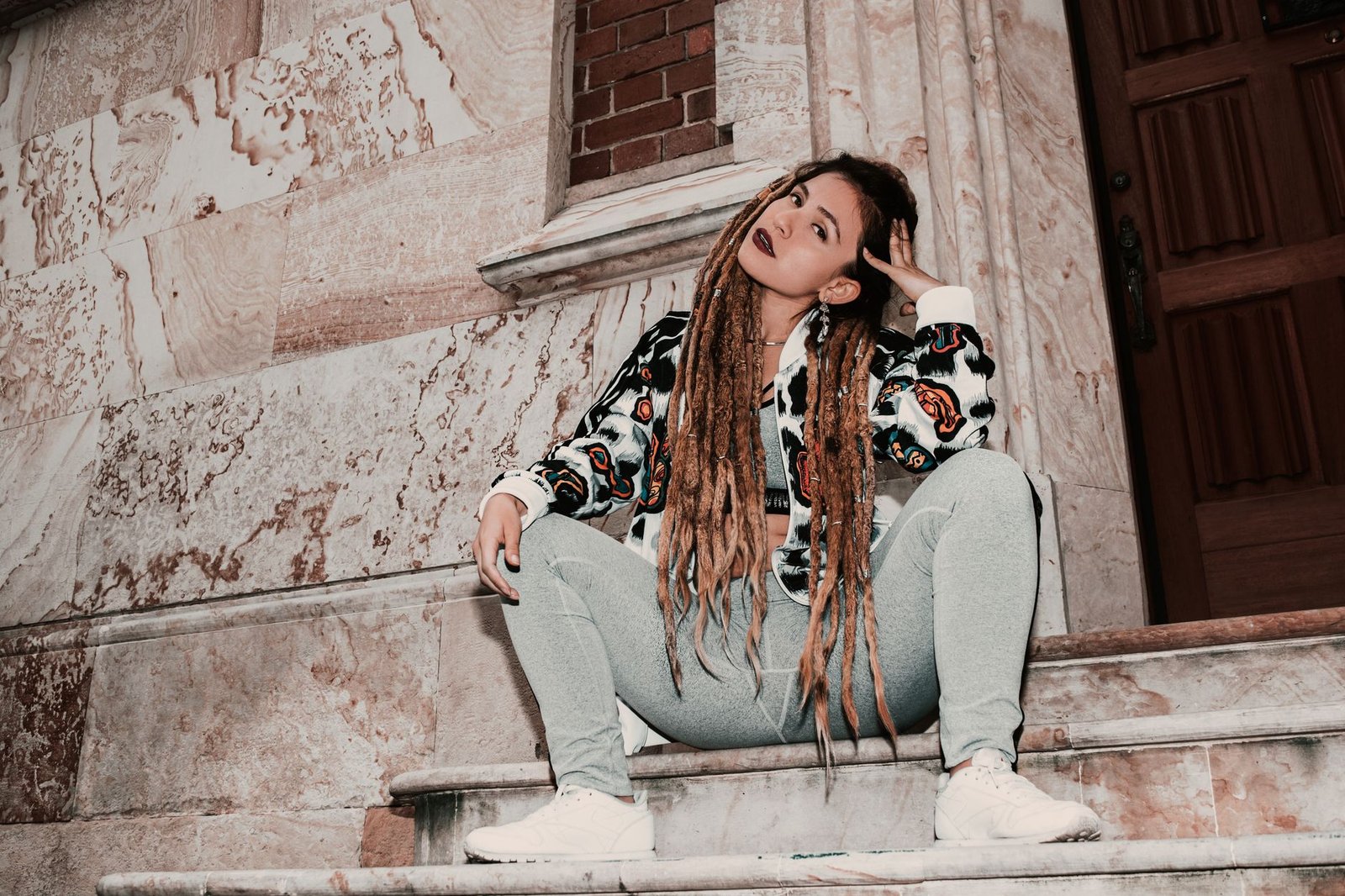 Fashionable woman with dreadlocks sitting on marble stairs in Bogotá, showcasing a modern urban look.