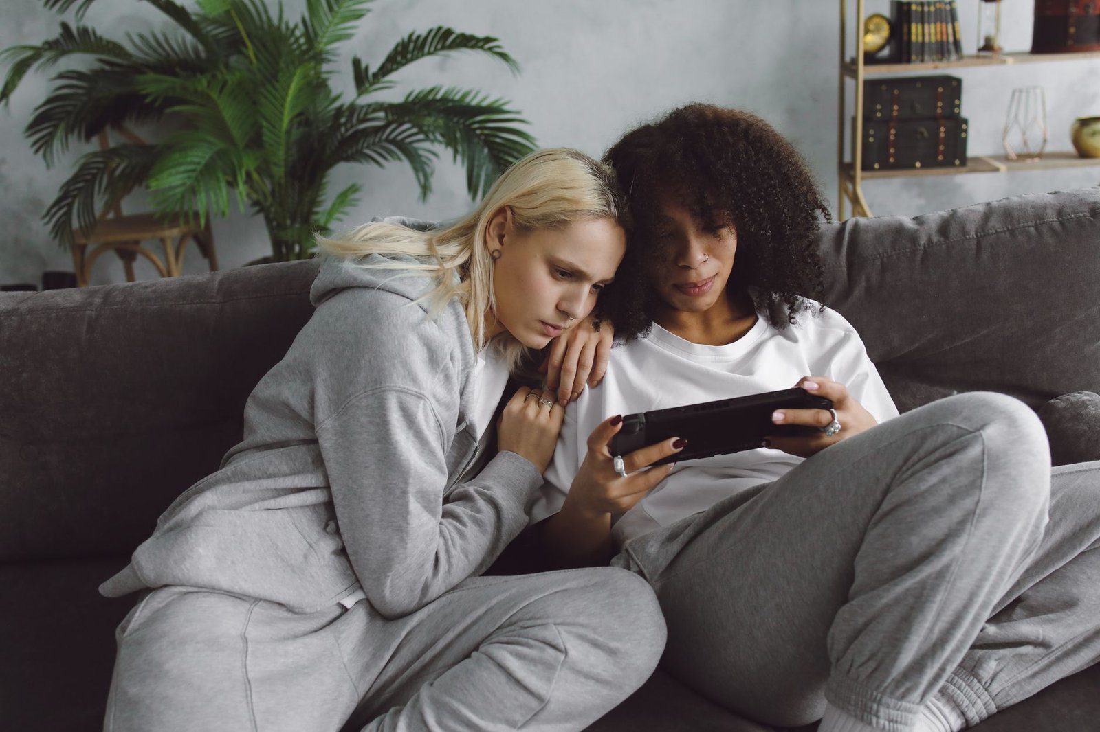 Two women relaxing on a couch while engaged with a digital tablet indoors.