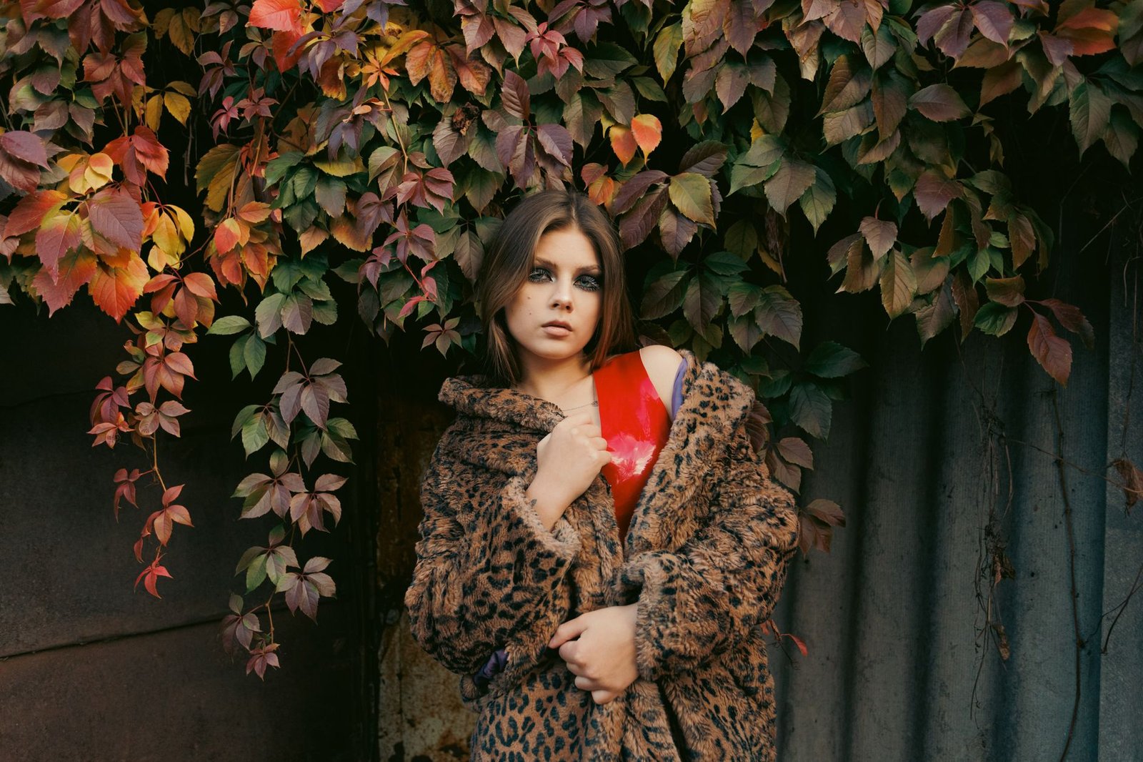 Stylish woman in leopard coat surrounded by vibrant autumn leaves.