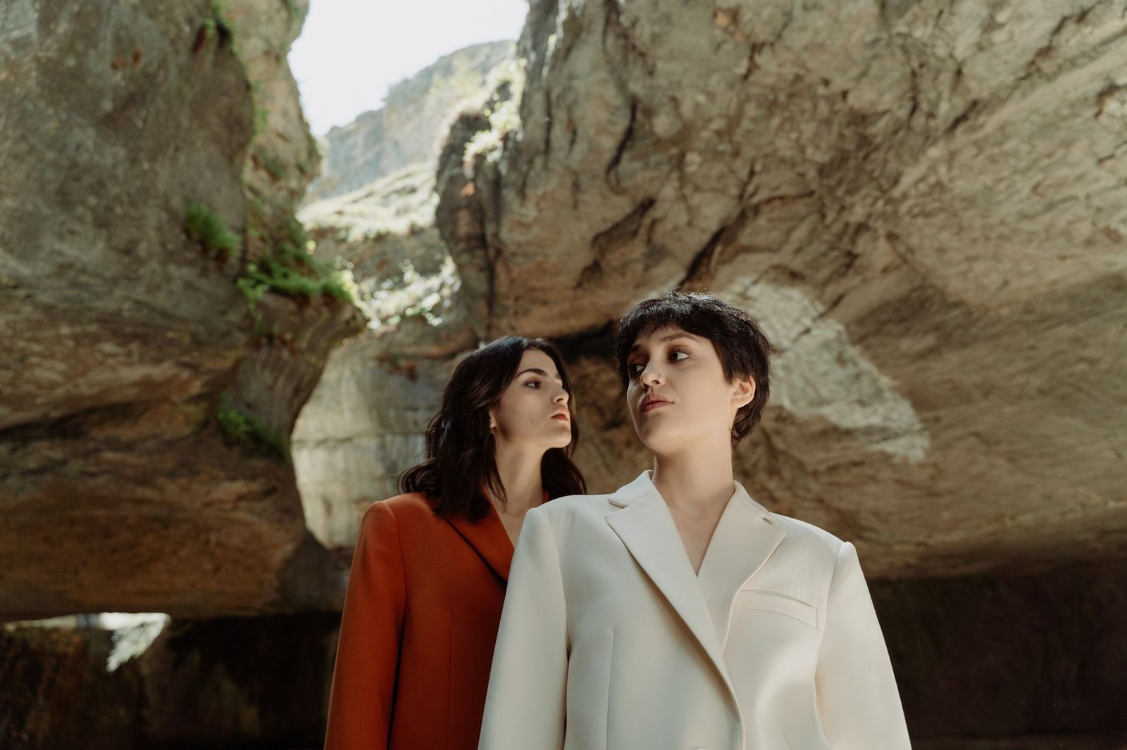 Two models showcase chic outfits in a dramatic rocky environment.