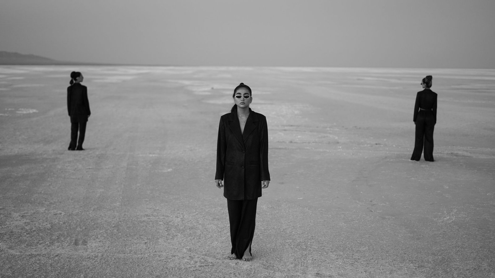 Three women in black suits standing in a desolate desert setting.