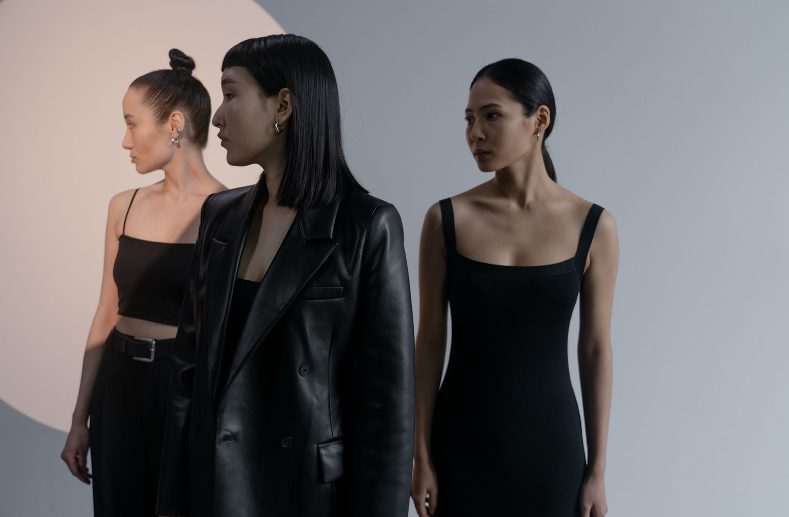 Three women in stylish black outfits pose elegantly against a studio backdrop.
