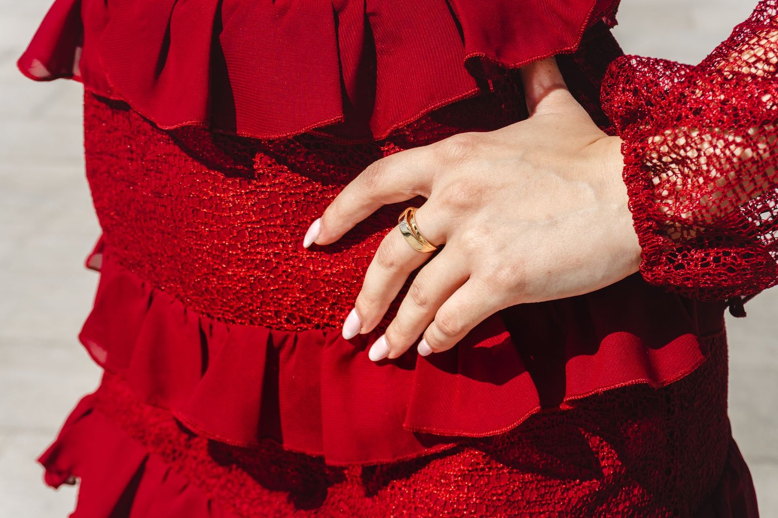Detailed view of a hand with ring resting on a textured red dress, showcasing elegance and style.