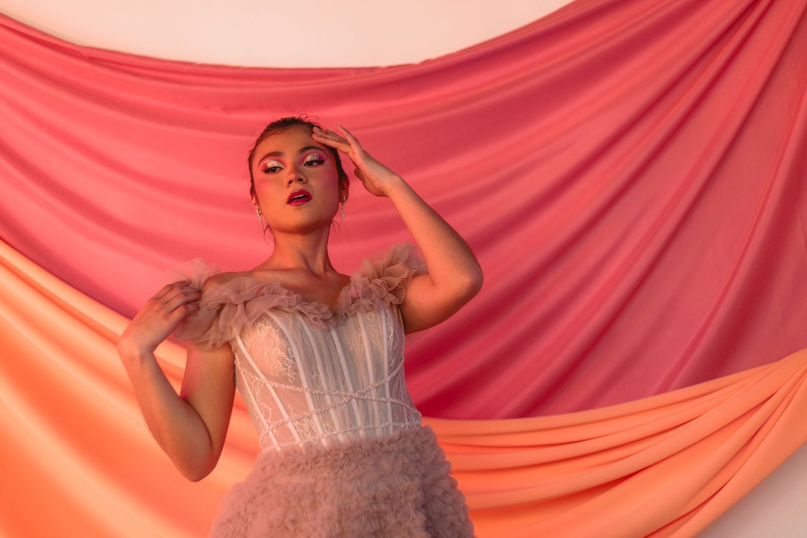 Model poses in a beautiful ruffled gown against pink draped background.