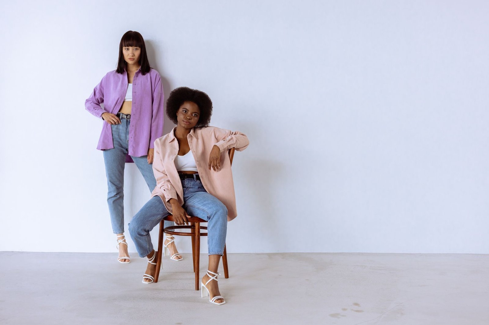 Two women in stylish, unbuttoned shirts posing against a neutral backdrop with ample copy space.
