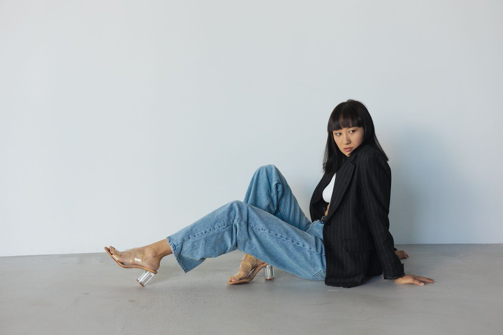 A fashionable woman poses in a black blazer and blue jeans with calm demeanor.