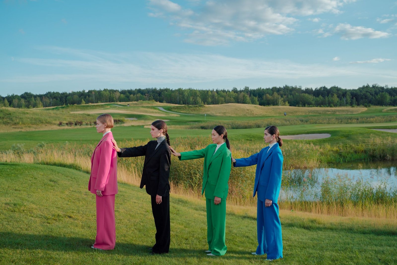 Group of stylish women in vibrant suits posing in a scenic outdoor setting.