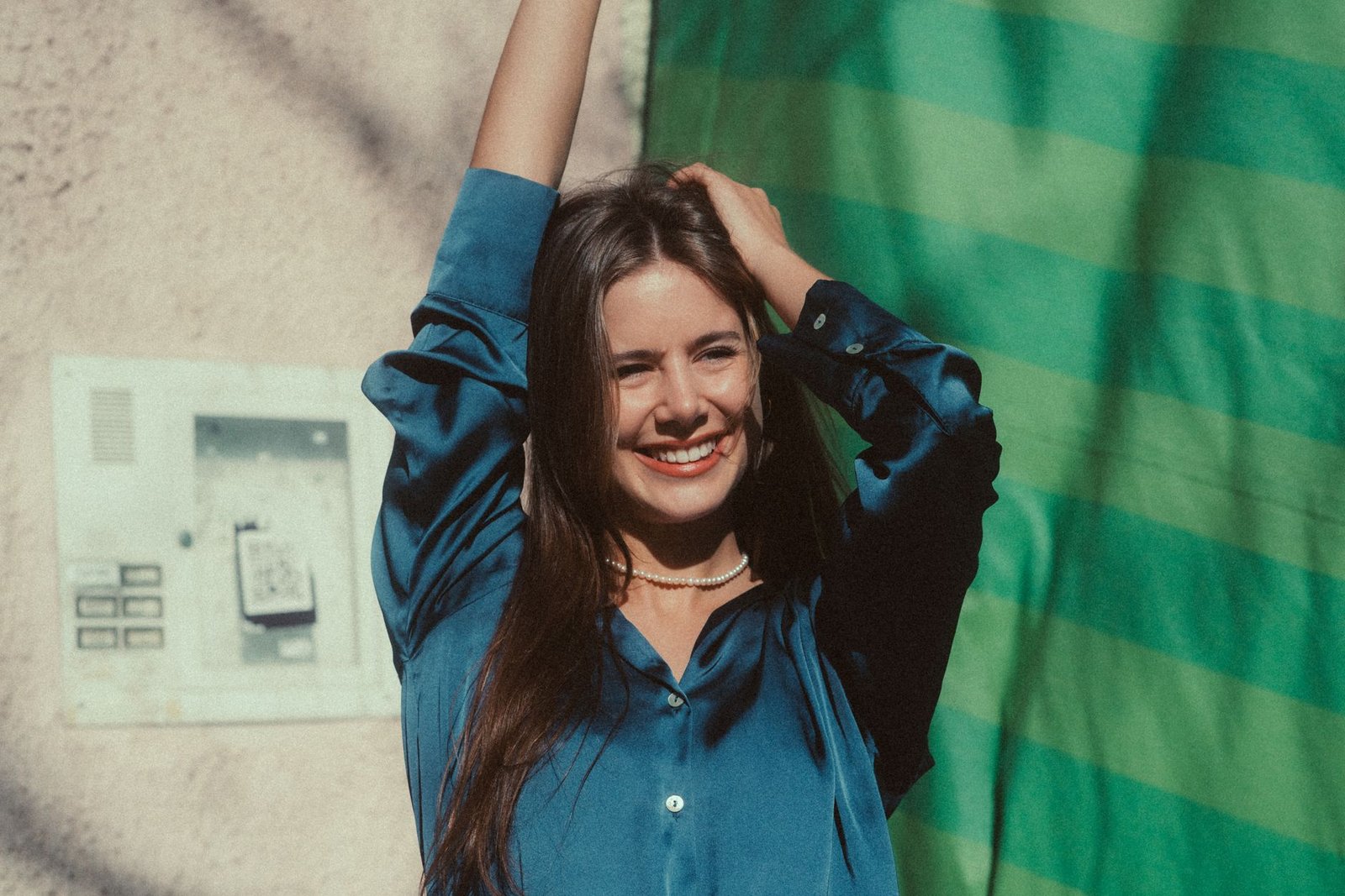 A young woman in a blue blouse smiles joyfully while standing outdoors, showcasing a vibrant and cheerful mood.